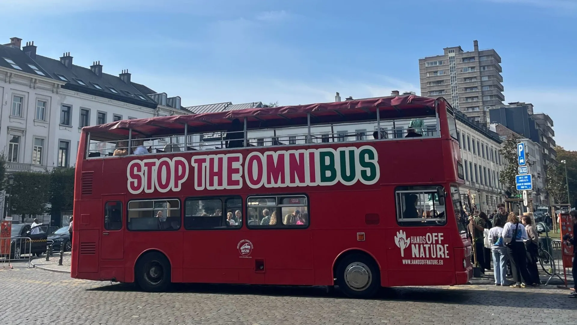 Ein roter Bus mit der Aufschrift Stop the Omnibus steht in Brüssel auf einer Straße.
